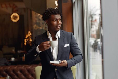 Black man standing in a cafe and drinking a coffeeの写真素材