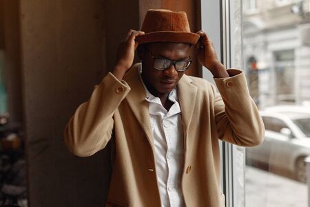 Black man in a brown coat standing by the windowの写真素材