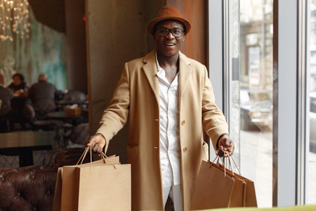 Black man standing in a cafe with shopping bagsの写真素材