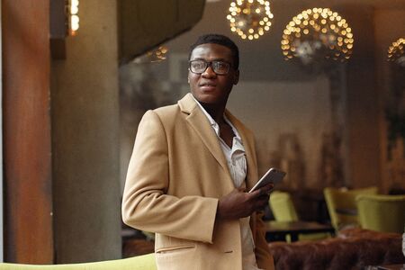 Black man in a brown coat standing with mobile phoneの写真素材