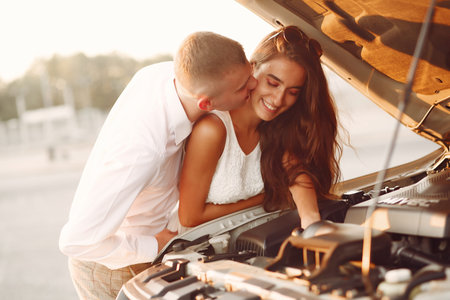 Beautiful couple spend time in a summer park near a car