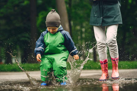 Funny kid in rain boots playing in a rain parkの写真素材