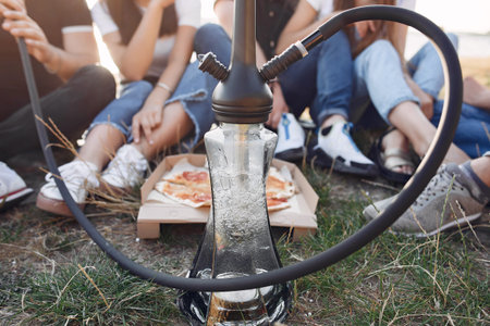 Young people eating pizza smoking shisha outside