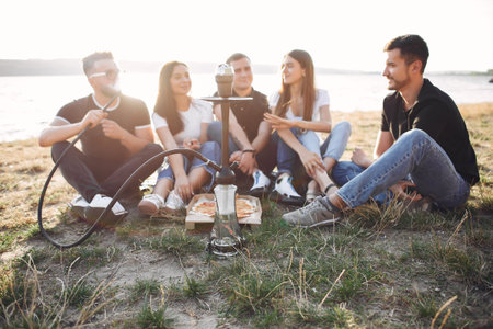 Young people eating pizza smoking shisha outside