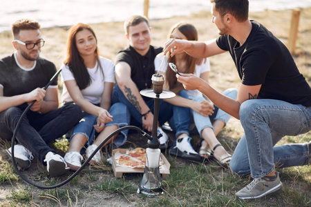 Young people eating pizza smoking shisha outside