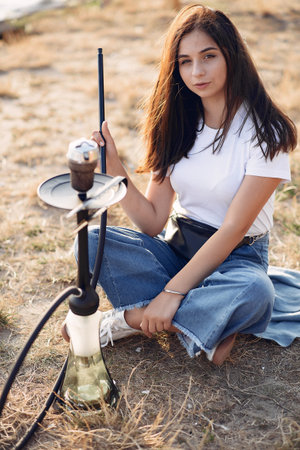 Woman holding pipe smoking shisha alone outside