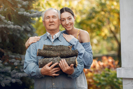 Grandfather with granddaughter on a yard with firewood in handsの写真素材