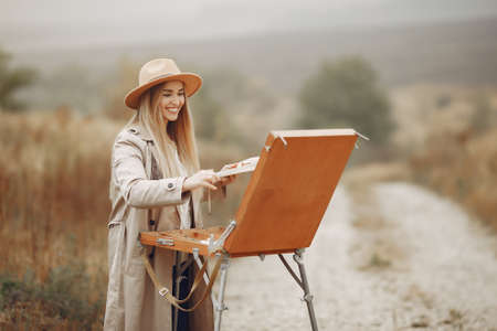 Woman in a brown coat painting in a fieldの写真素材