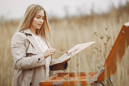 Woman in a brown coat painting in a field