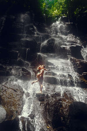 Couple stand under a large waterfallの写真素材