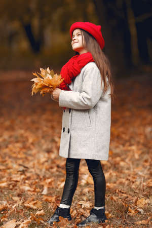 Cute little girl in a gray coat playing in a autumn parkの写真素材