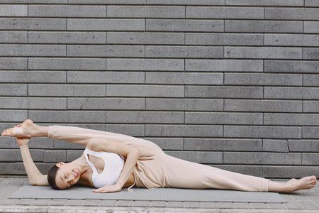 Woman practicing advanced yoga against a dark urban wall