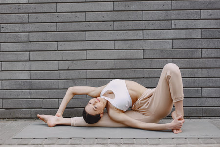 Woman practicing advanced yoga against a dark urban wall