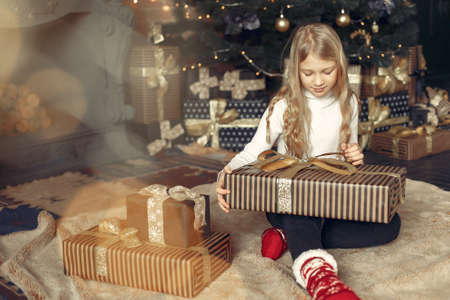 Little girl in a white sweater near christmas tree with presentの写真素材
