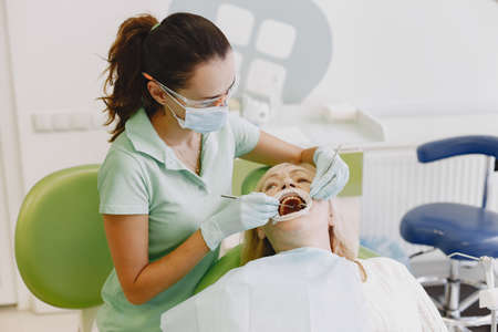 Dentist looking her old patient with toolsの写真素材