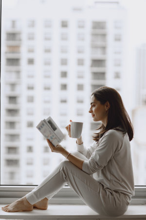 Brunette sitting on a windowsill and drinks a coffeeの写真素材