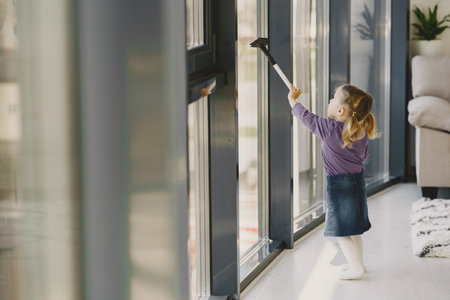 Little girl cleaning windows with vacuum cleanerの写真素材