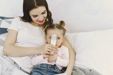 Mother with thermometer is sitting near daughter