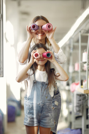 Mother with little daughter standing at the fabric with threadの写真素材