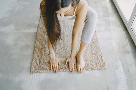 Girl doing yoga exercises at home near sofa and window in sportswearの写真素材