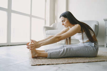 Girl doing yoga exercises at home near sofa and window in sportswearの写真素材