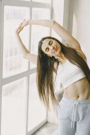 Girl doing yoga exercises at home near sofa and window in sportswear