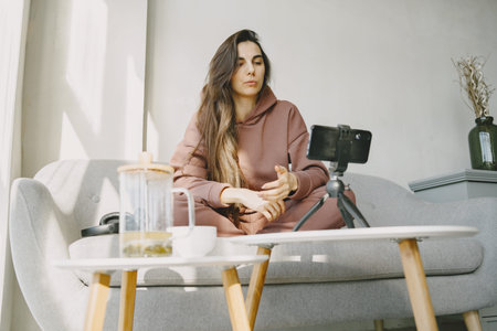 Woman at home with headphones and phone communicates onlineの写真素材