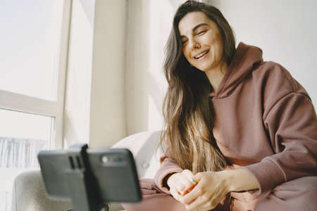 Woman at home with headphones and phone communicates onlineの写真素材