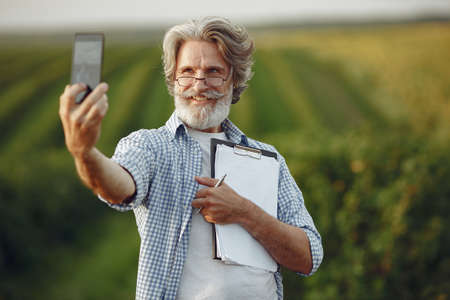 Old farmer in shirt standing on field with notebookの写真素材