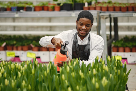 African guy works in garden and waters flowers
