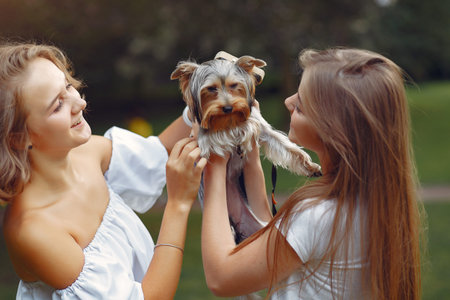 Two cute girls in a park playing with little dogの写真素材