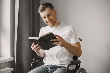 Handicapped man in wheelchair reading a book at homeの写真素材