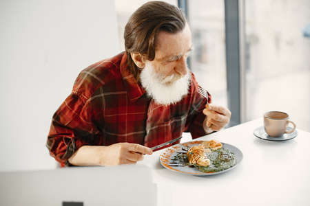 Senior man sitting in kitchen eating dinnerの写真素材