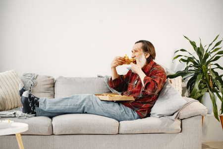 Senior casual man eating pizza on couchの写真素材