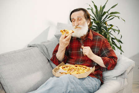 Senior casual man eating pizza on couchの写真素材