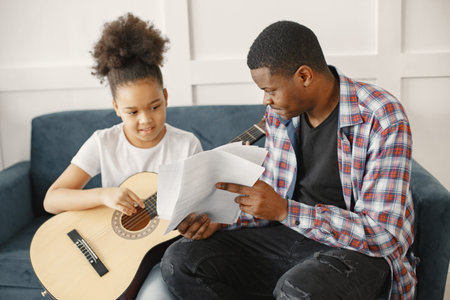 African father teaches his daughter to play guitarの写真素材