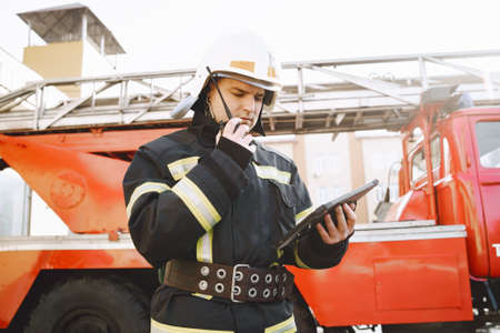 Male firefighter with tablet in uniform on car backgroundの写真素材