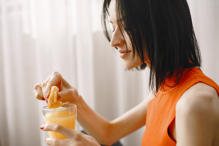 Girl in an orange jacket sits on floor and drinks juice