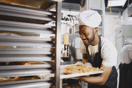 African American baker in uniform sorting baked products on palletsの写真素材