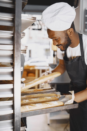 African American baker in uniform sorting baked products on pallets