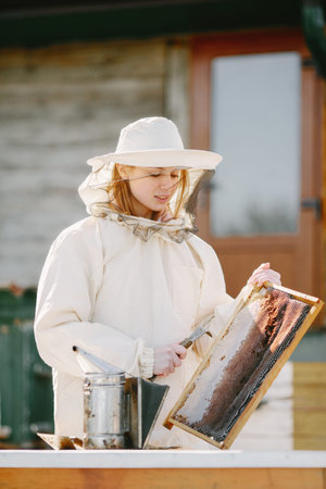 Female beekeper in uniform collecting honey from combs