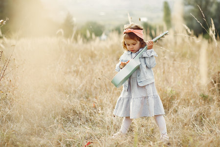 Cite little girl in a autumn park playing on a guitarの写真素材