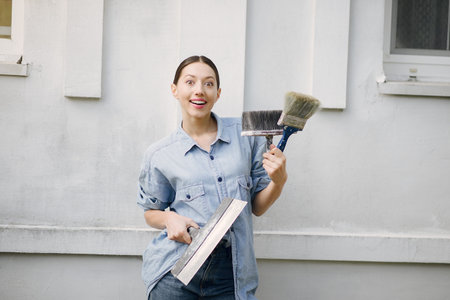 Cute girl standing near wall with repair tools