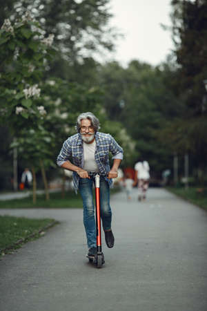 Portrait of elderly man with kick scooter in a summer parkの写真素材