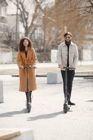 Interracial young couple with scooters in the city background