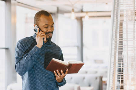 Man sitting in a cafe and talking on the phone, holding a notebook.の写真素材
