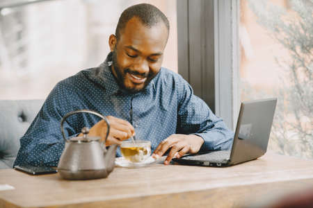 Man sitting in a cafe and working behind a laptop, writing in a notebook and drink a tea.の写真素材