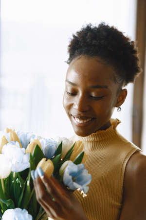 African girl with a bouquet of flowers by windowの写真素材