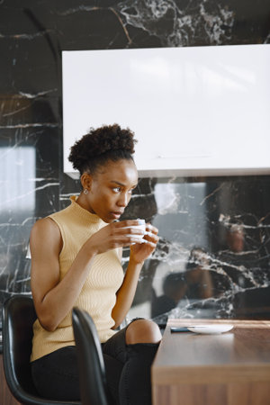 African girl drinks coffee in kitchen by windowsの写真素材