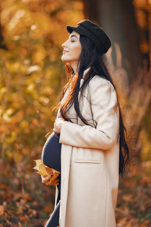 Pregnant woman in a brown coat in a autumn parkの写真素材